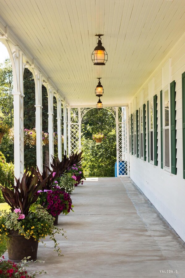 A covered porch with white columns, hanging lanterns, and potted plants.