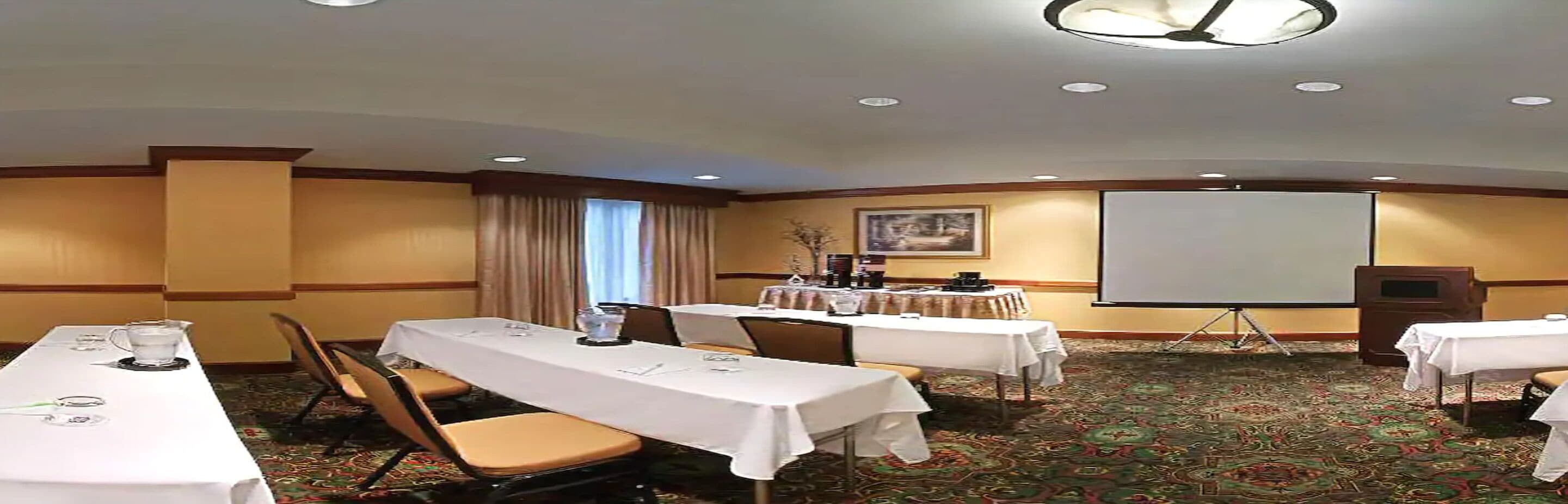 A conference room with multiple tables, chairs, a projector screen, and a carpeted floor.