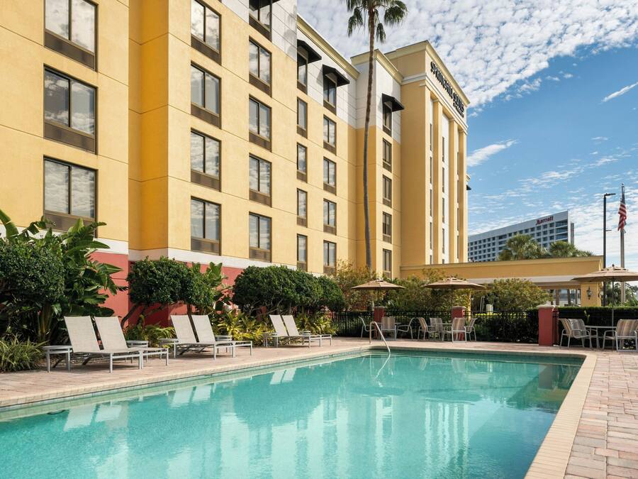 A hotel with a swimming pool, lounge chairs, and an outdoor seating area with umbrellas.