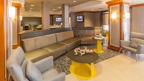 A modern hotel lobby with a large sectional sofa, a yellow coffee table, and a seating area with armchairs. - SpringHill Suites by Marriott Tampa Westshore Airport (Tampa)