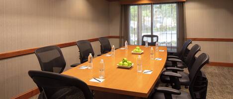 A conference room with a long table, chairs, water bottles, and a fruit bowl.