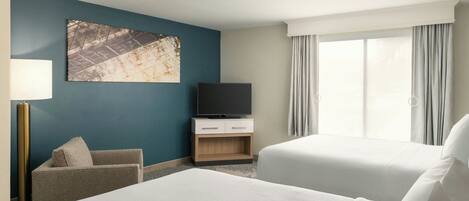 A hotel room with two beds, a TV on a wooden cabinet, a chair, and a large window with curtains.