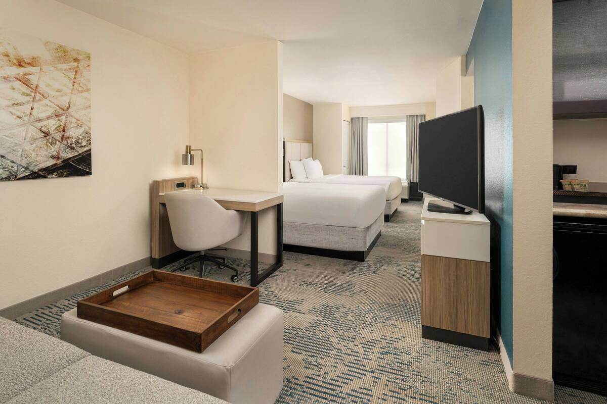 A hotel room with a desk, two beds, a TV, and a large abstract painting on the wall.