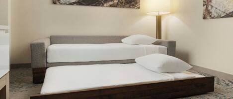 A hotel room with a double bed, a sofa bed, a lamp, and abstract wall art.