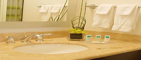 A bathroom with a marble sink, three faucets, a mirror, and a towel rack with white towels.