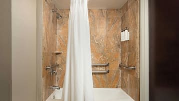 A bathroom with a shower, a bathtub, marble walls, and handrails.