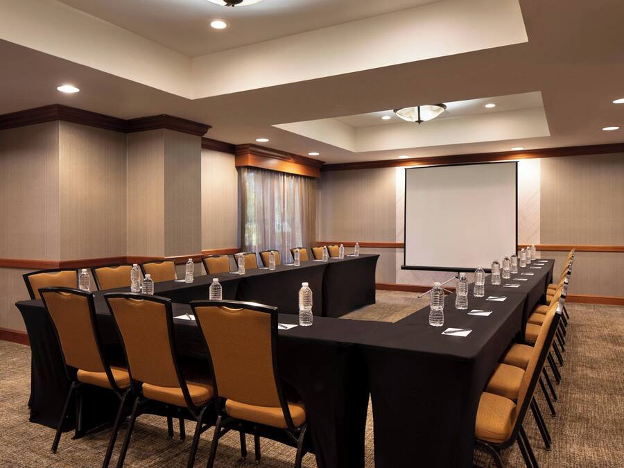 A conference room with a long table, chairs, and a projector screen.
