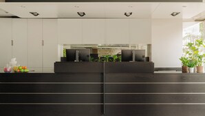 A reception desk with a dark wood finish, a glass partition, and a potted plant on the right.