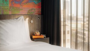 A hotel room with a bed, a small table with a jar of candies, a book, and a wall art piece.