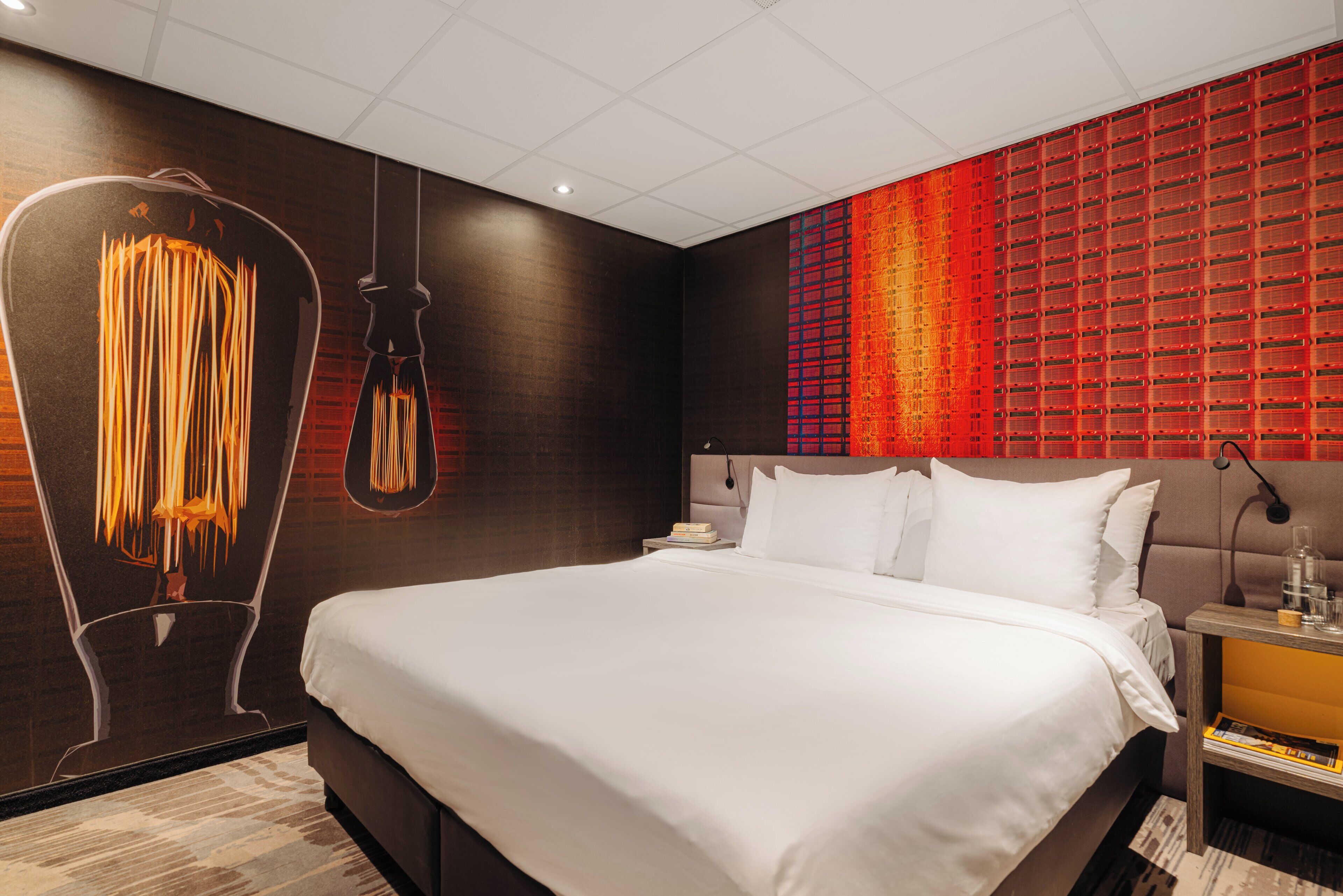 A modern hotel room with a large bed, a unique wall art installation, and a red patterned wall.