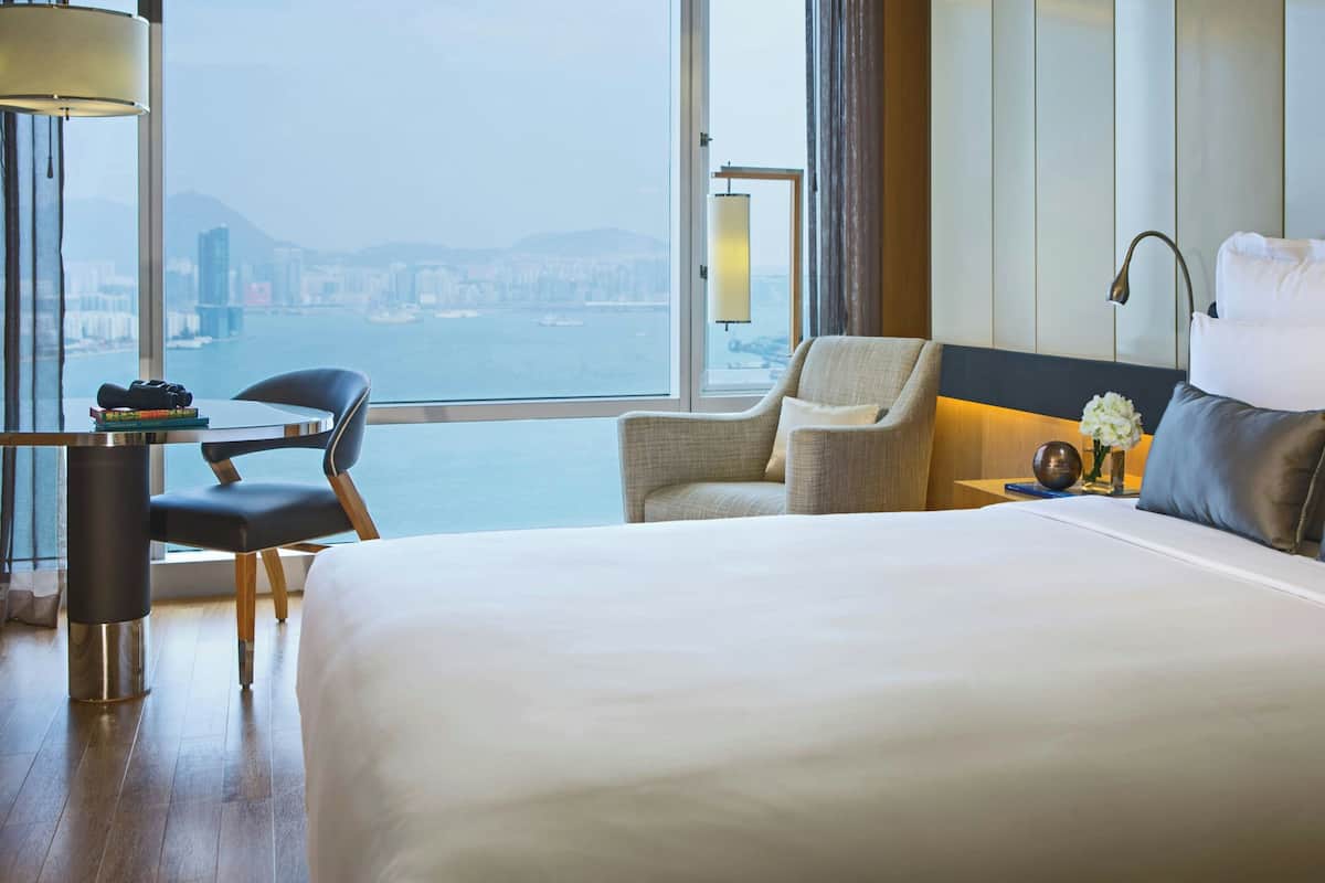 A hotel room with a large bed, a chair, a small table, and a view of the city and water.