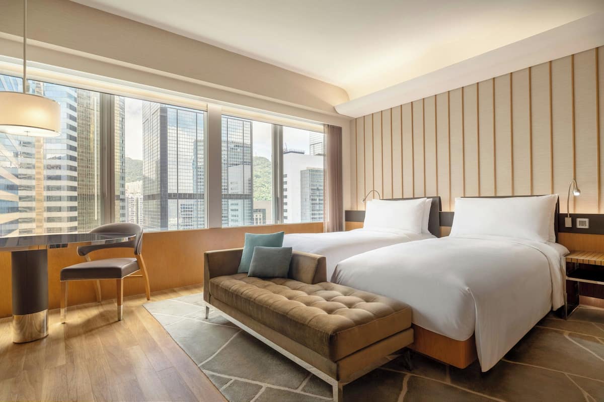 A modern hotel room with a large window, a sofa, a bed, and a desk.