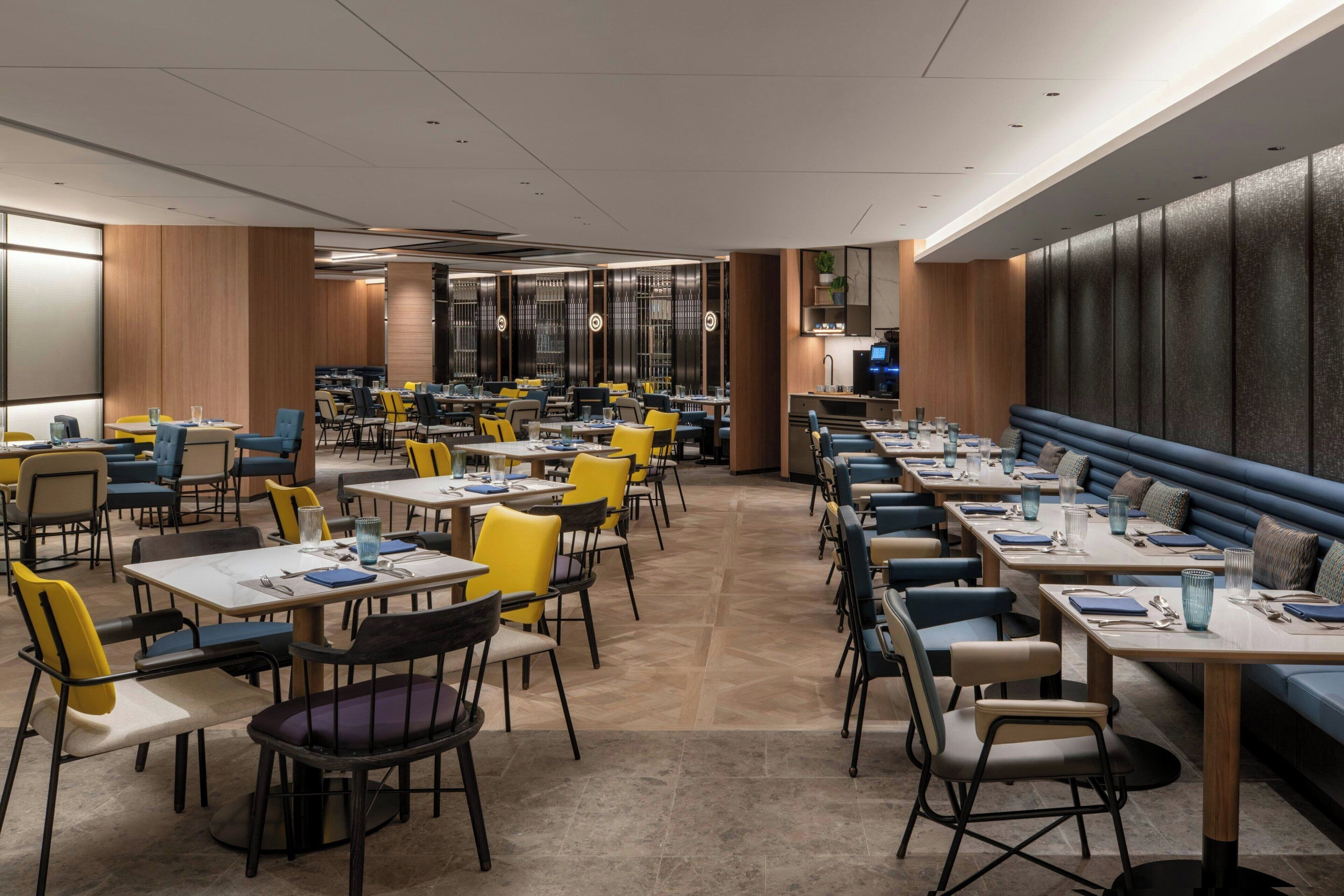 A modern dining area with multiple tables and chairs, a long counter, and a seating area with a cushioned bench.