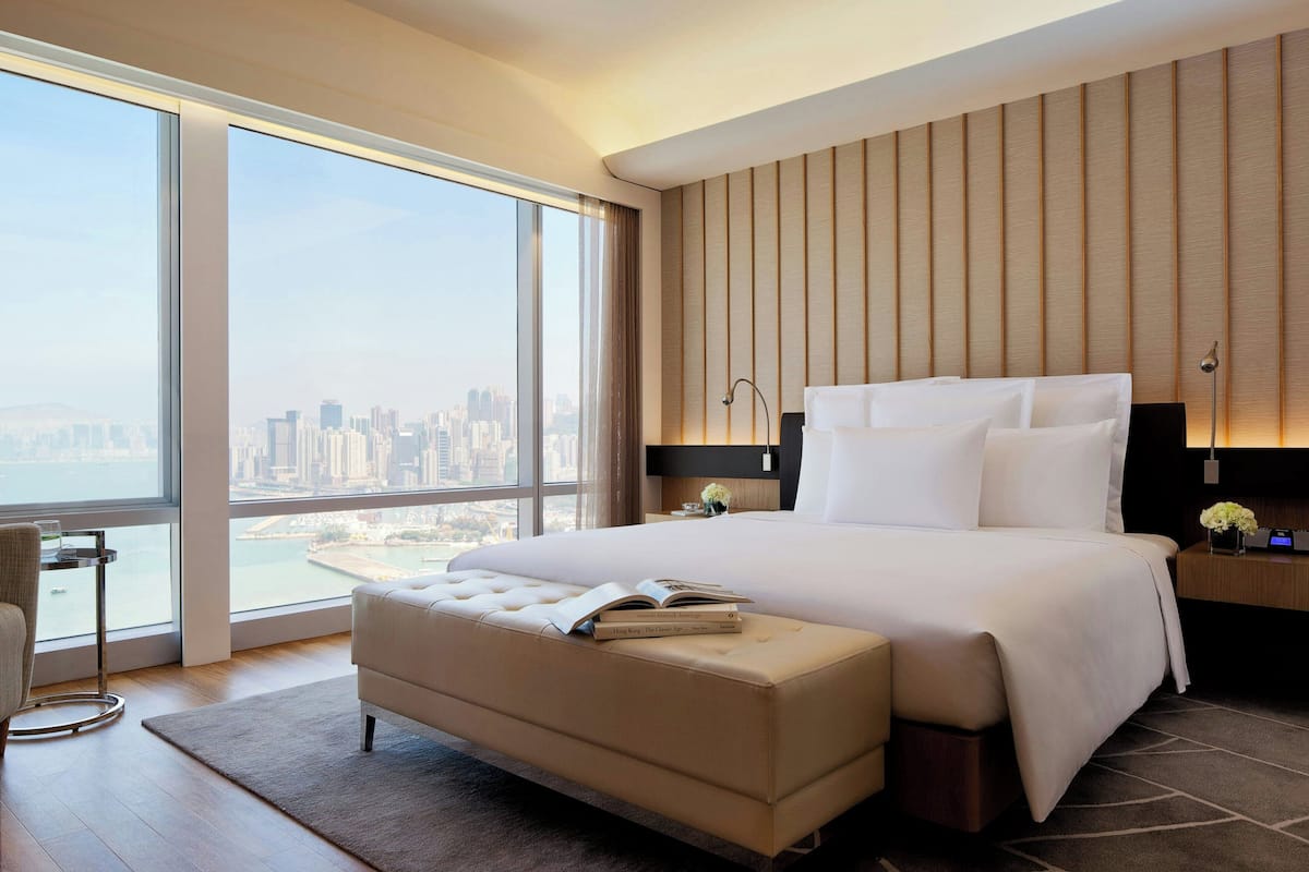 A modern hotel room with a large bed, a view of the city, and a city skyline visible through the window.