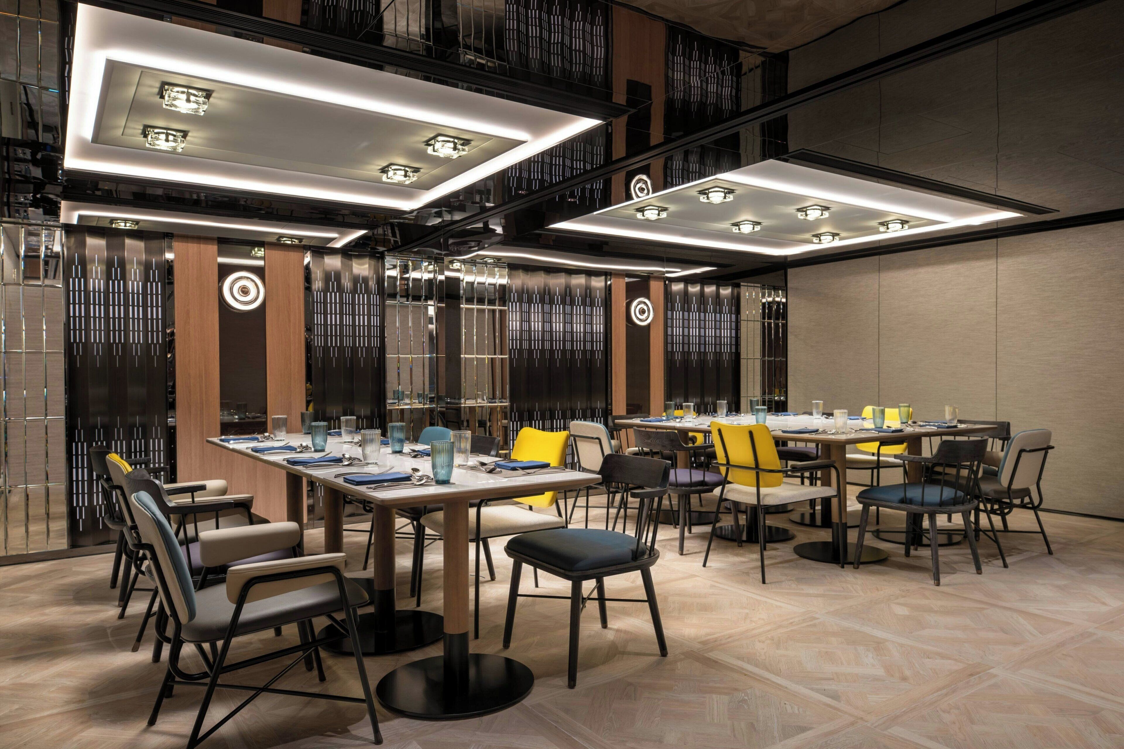 A modern conference room with multiple tables and chairs, equipped with overhead lighting and a decorative wall panel.