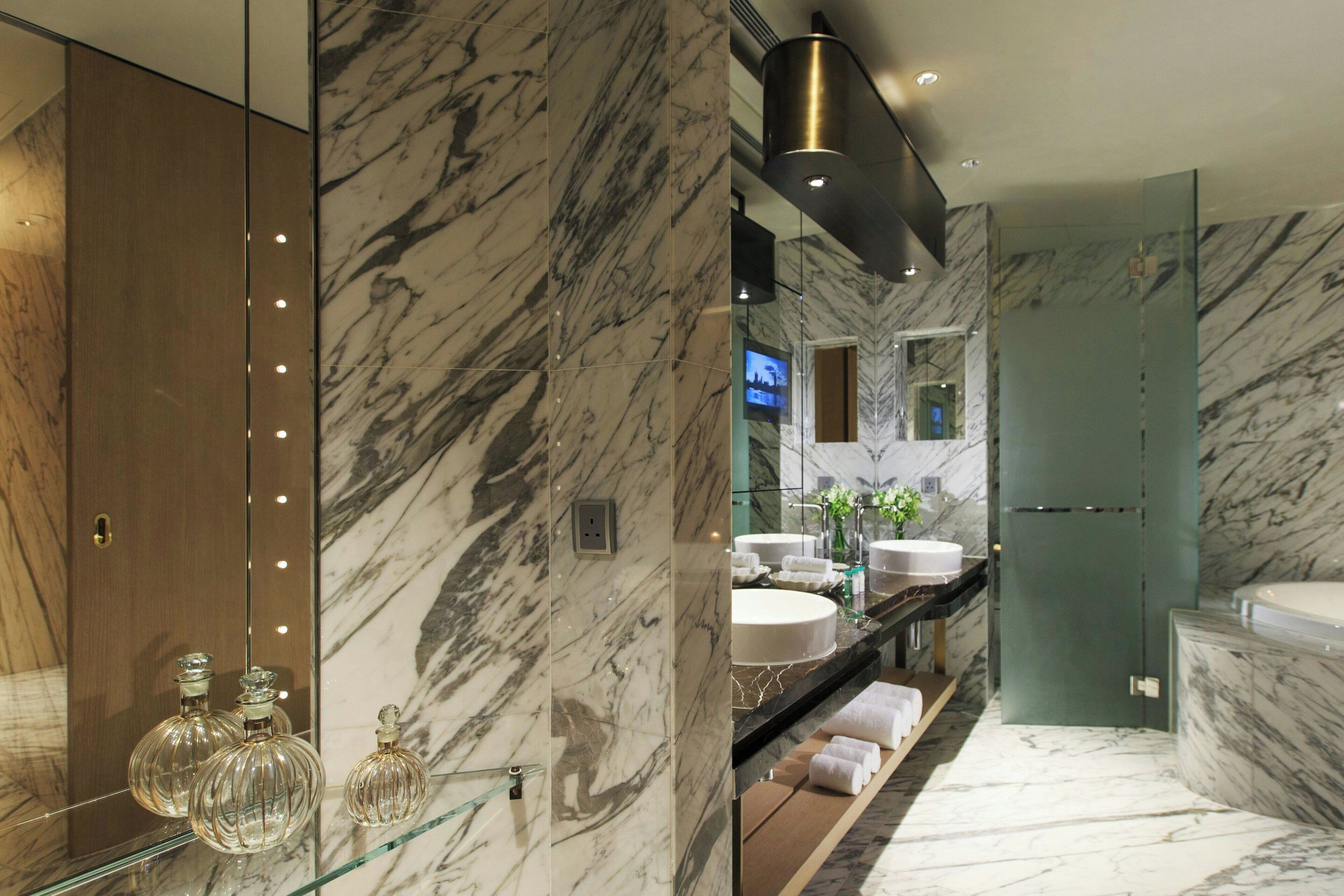 Un baño moderno con paredes de mármol, cabina de ducha de vidrio y tocador doble.
