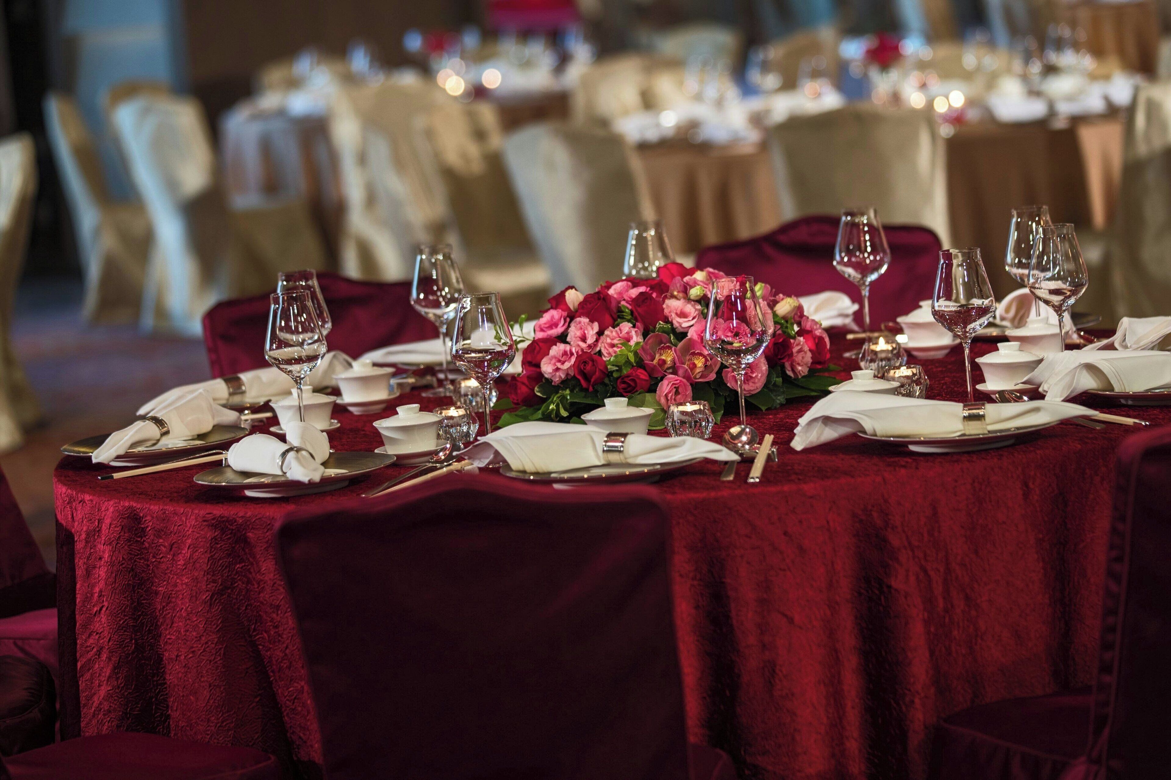 A table set for a formal dining experience with red tablecloths, white napkins, and a centerpiece of pink flowers.
