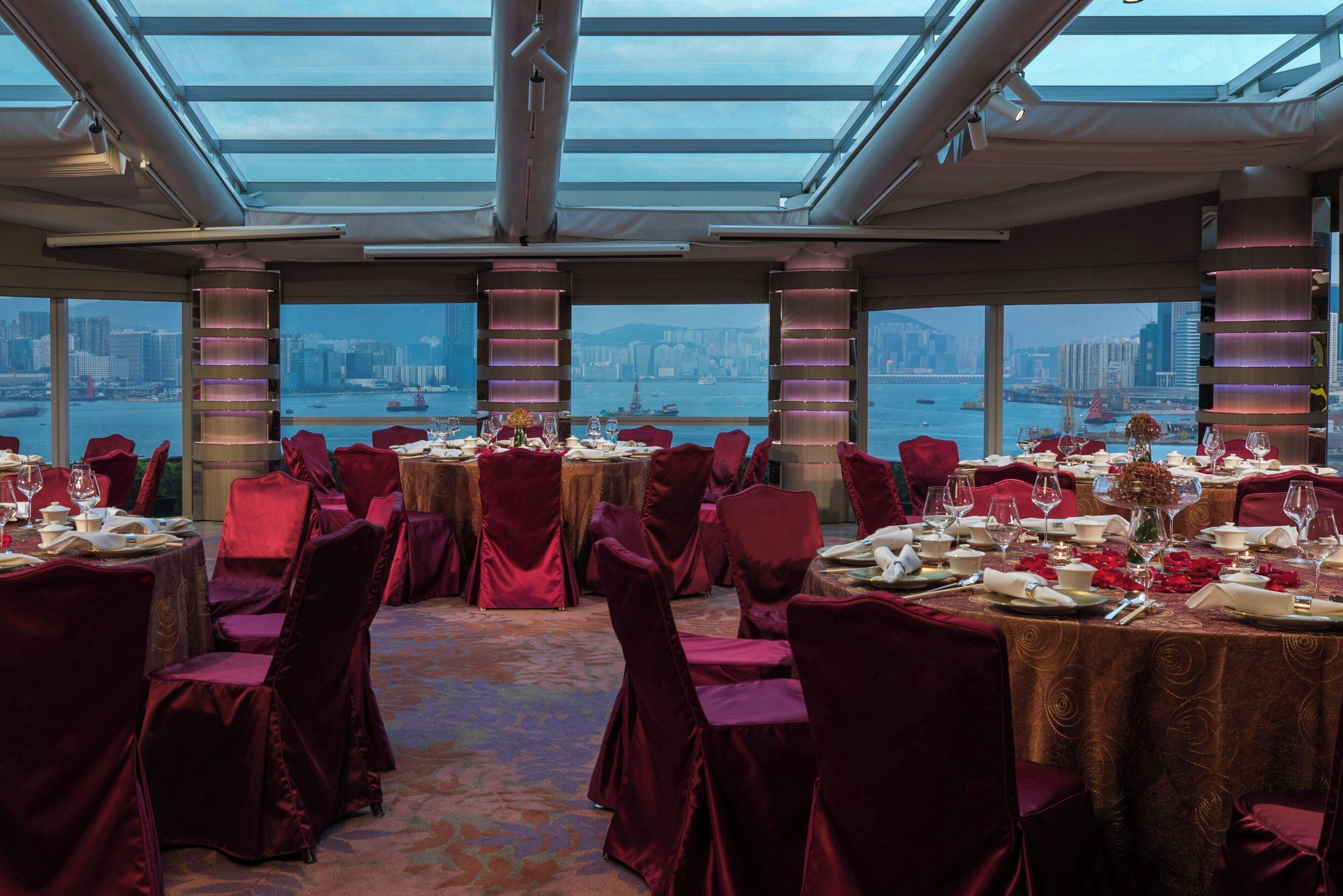 A dining area with round tables, red velvet chairs, and a view of a cityscape through large windows.