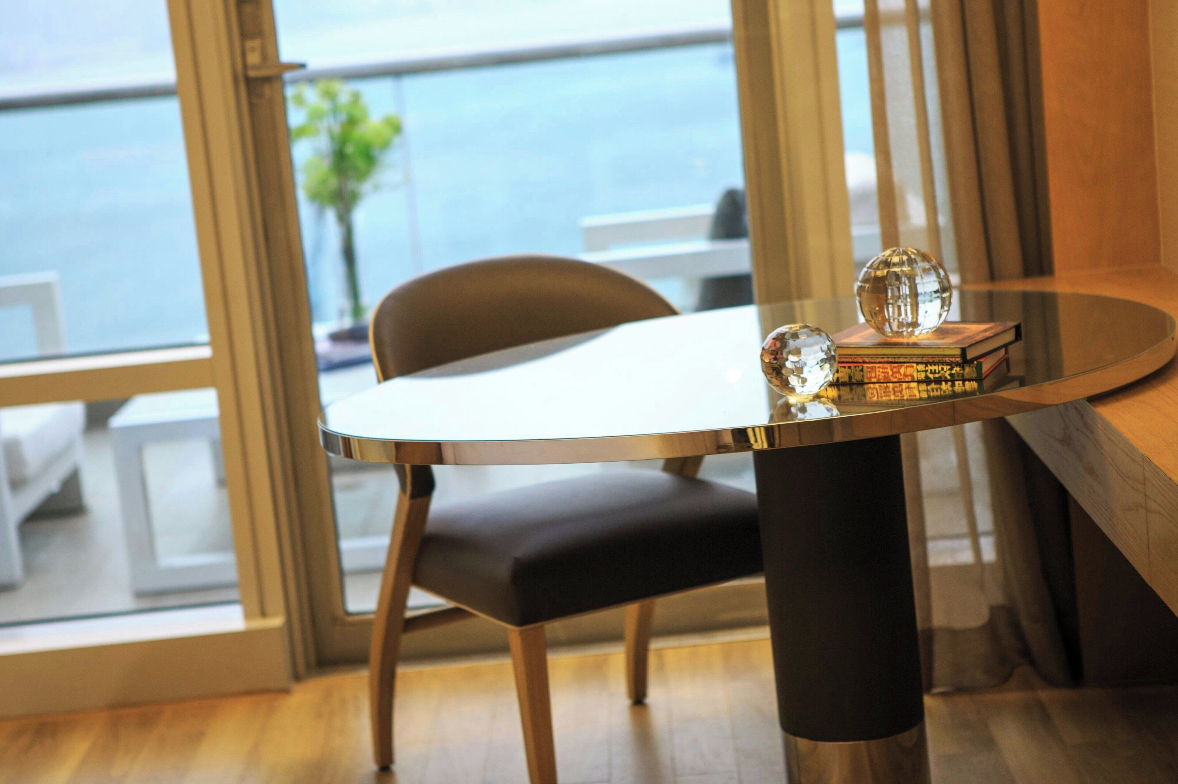 Un comedor moderno con una mesa redonda, una silla tapizada en negro y vistas al mar a través de amplios ventanales.