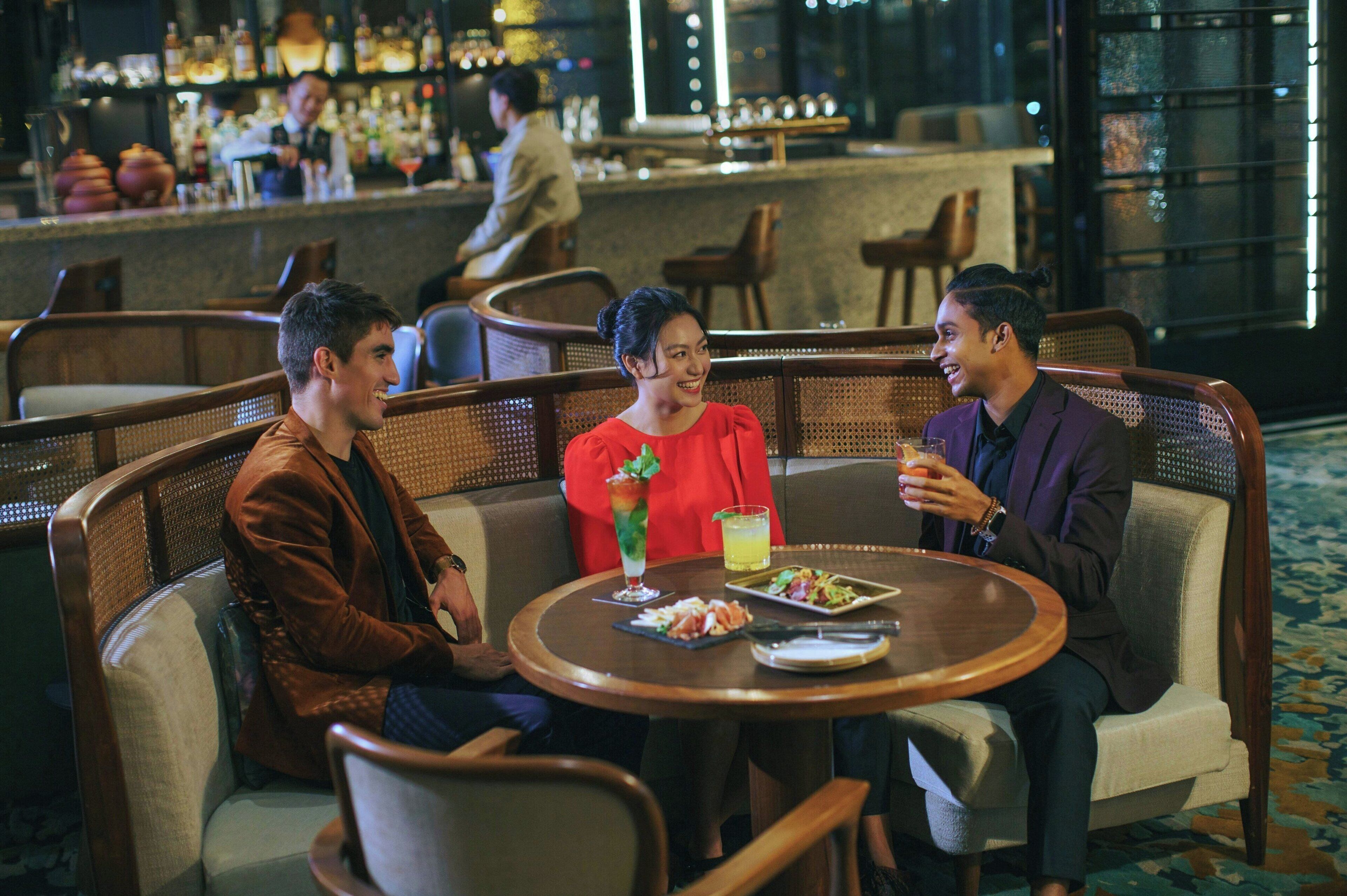 A group of three people seated at a round table in a restaurant with a bar in the background.