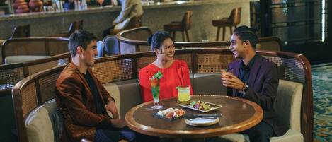 A group of three people seated at a round table in a restaurant with a bar in the background.