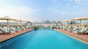 A rooftop pool with lounge chairs and umbrellas, offering a city skyline view.
