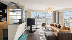 A modern living room with a sofa, a coffee table, and a TV. There is a city view through large windows.