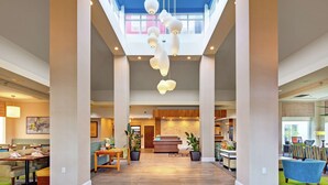 A spacious lobby with a high ceiling, a reception desk, seating areas, and a view of the sky through large windows. - Hilton Garden Inn Toronto/Oakville (Oakville)