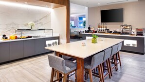 A modern kitchen with a marble backsplash, a large island with bar stools, and a flat-screen TV mounted on the wall. - Hilton Garden Inn Toronto/Oakville (Oakville)