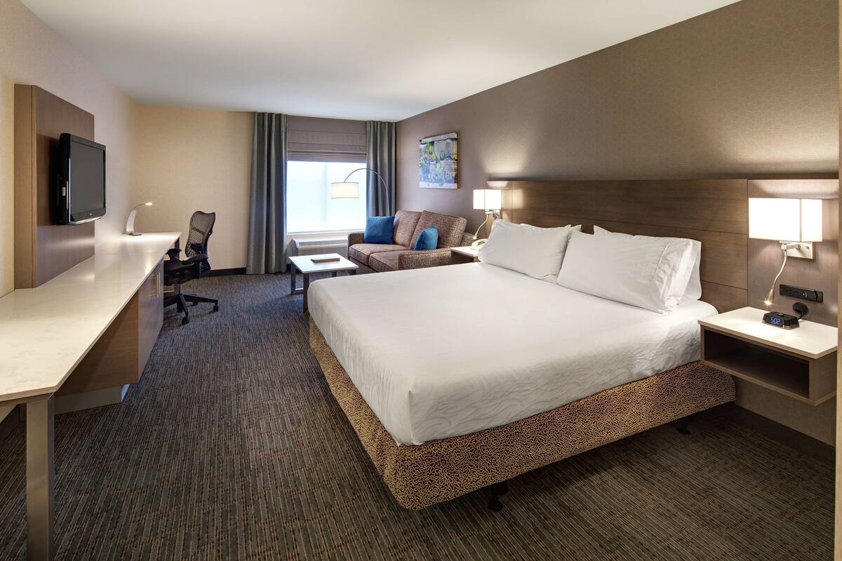 Habitación de hotel con una cama grande, un escritorio con computadora, una silla y un televisor.