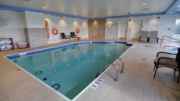 A pool area with a tiled floor, poolside chairs, and a lifebuoy on the wall.