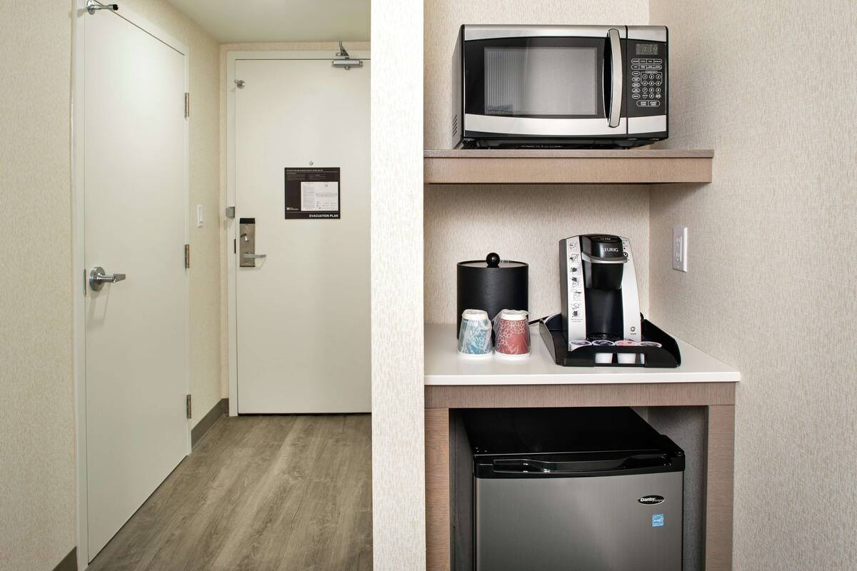Una kitchenette compacta equipada con microondas, cafetera y lavavajillas.