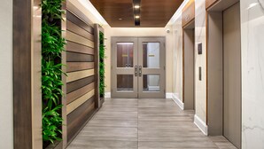 A hallway with wooden paneling, green plants, and a marble floor leading to double doors with glass panels and a control panel. - Hilton Garden Inn Toronto/Oakville (Oakville)