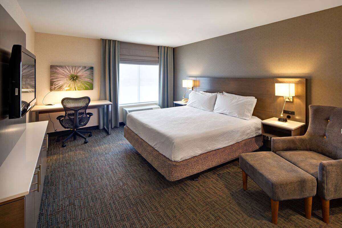 Una habitación de hotel con una cama grande, un escritorio con una silla, un televisor y dos lámparas de noche.