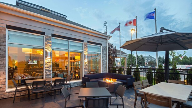 An outdoor patio with seating, a fire pit, and a view of the restaurant inside. - Hilton Garden Inn Toronto/Oakville (Oakville)