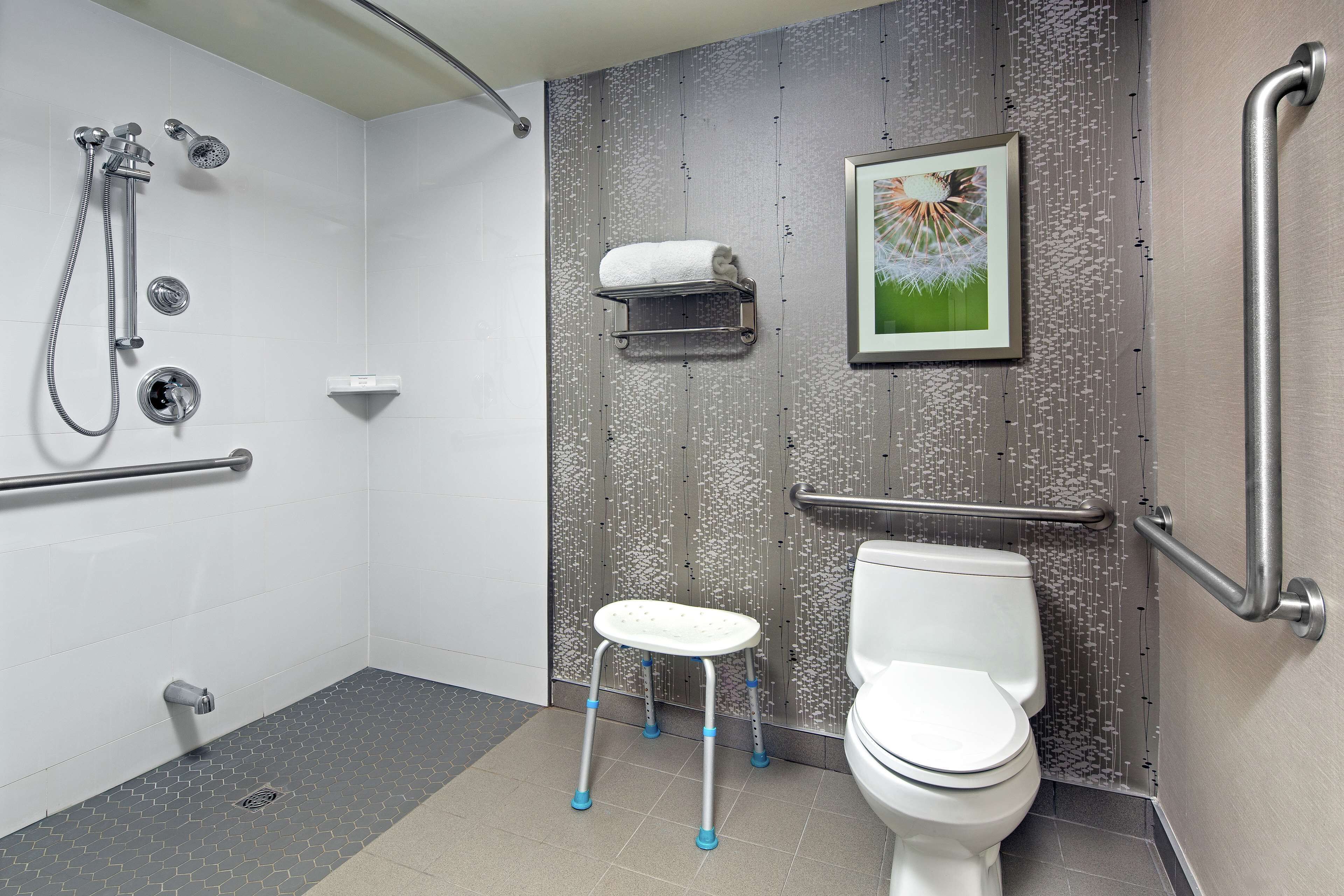 Ein modernes Badezimmer mit Dusche, Toilette und Haltegriffen.