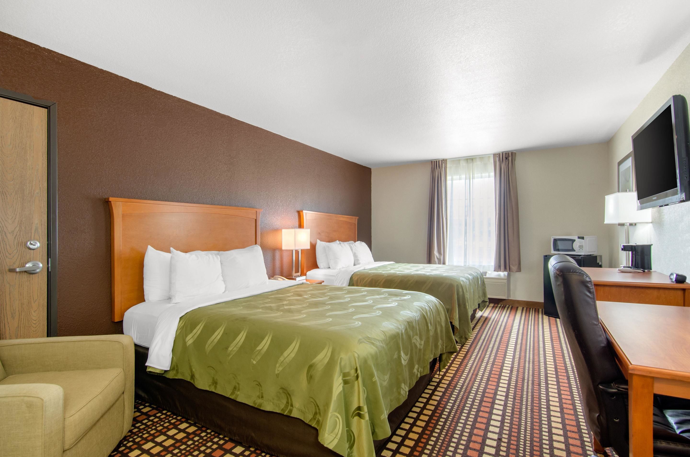 A hotel room with two beds, a desk, a chair, a television, and a microwave.