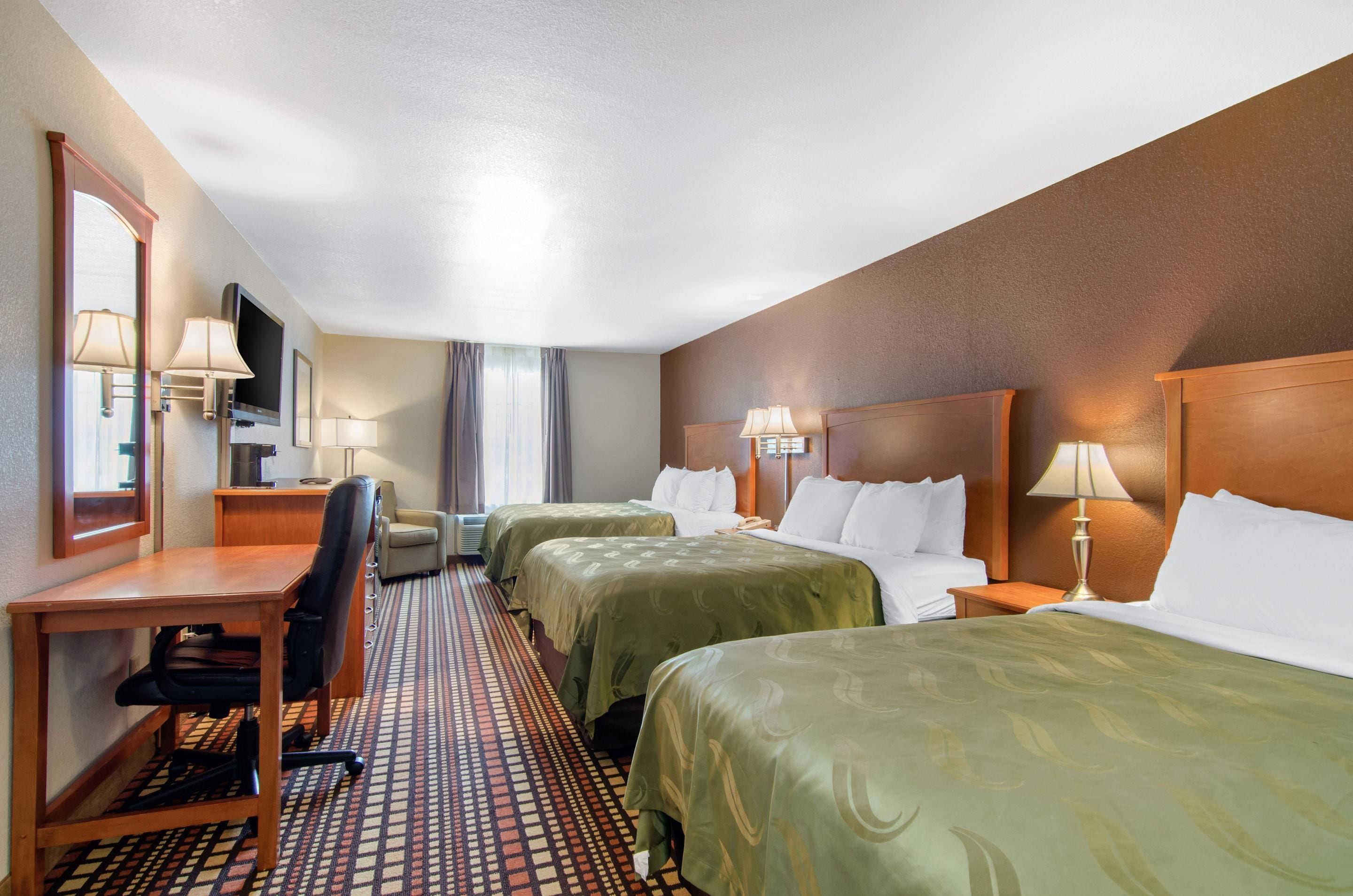 A hotel room with two beds, a desk, a chair, a TV, and a window with curtains.