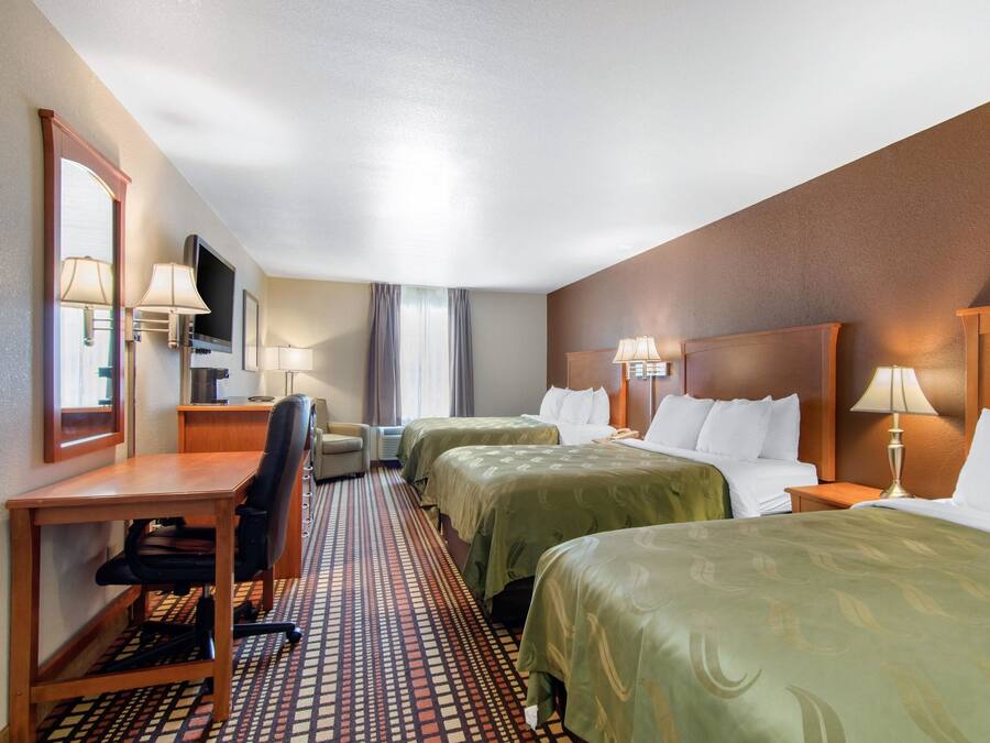 A hotel room with two beds, a desk, a chair, a TV, and a window with curtains.