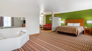 A hotel room with a large bed, a separate bathroom with a bathtub, a red sofa, and a patterned carpet. - Quality Inn Kearney - Liberty (Kearney)