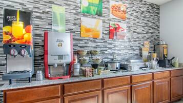 A hotel kitchen with a fruit juice dispenser, a coffee maker, and various kitchen appliances.