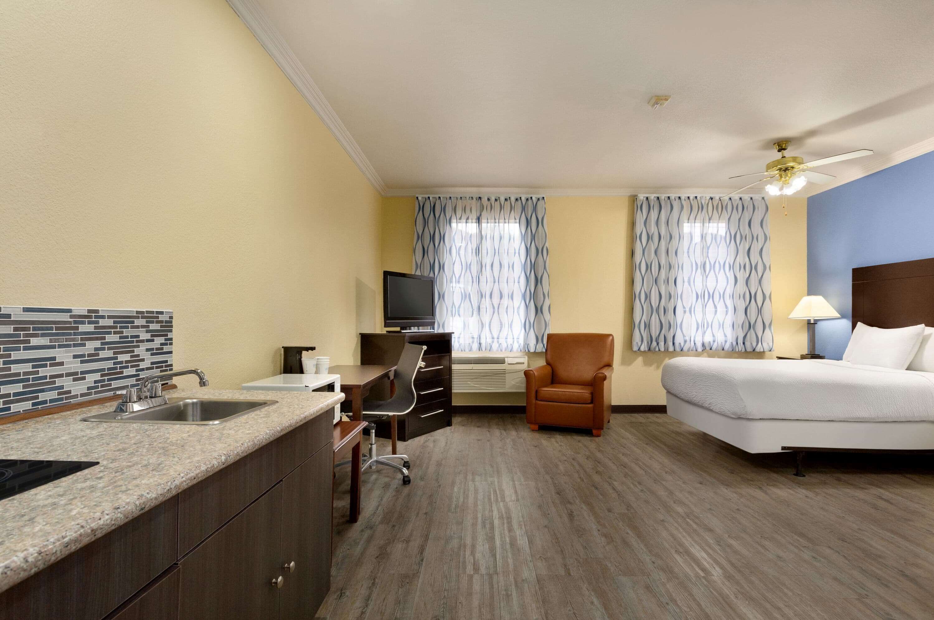 A hotel room with a kitchenette, a bed, a desk with a chair, and a TV.
