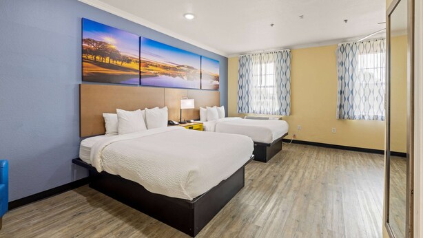 Une chambre d’hôtel avec deux lits, un grand tableau au mur et une fenêtre ornée de rideaux à motifs.