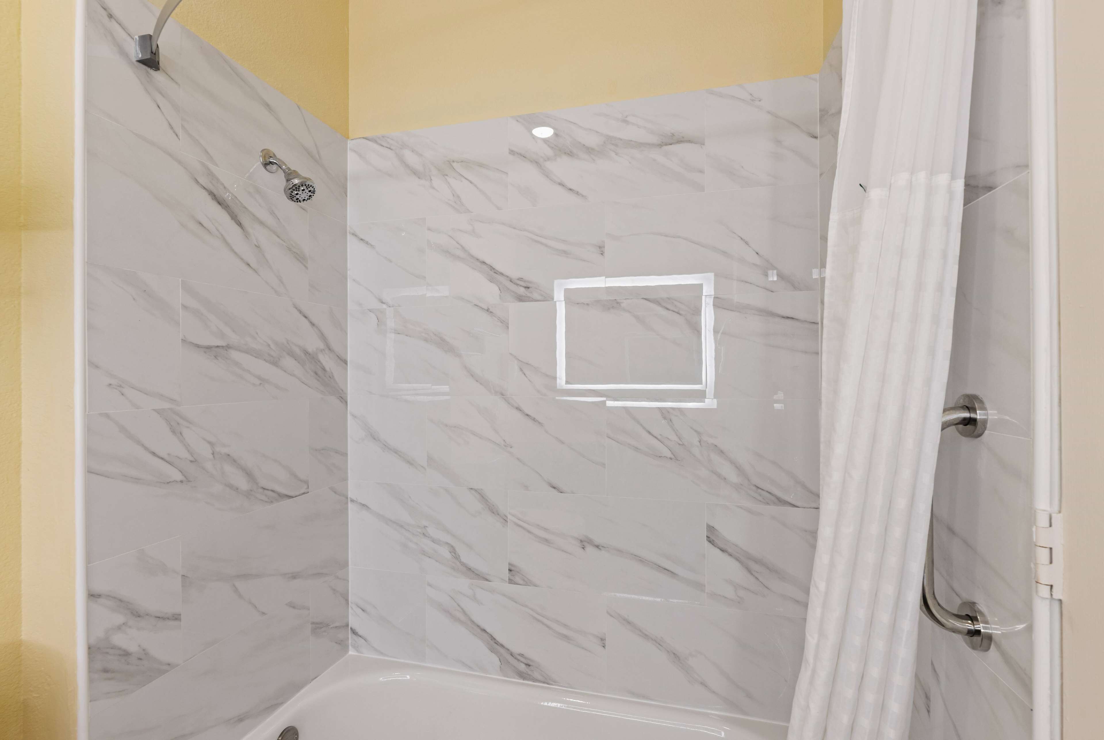 A bathroom with a shower area featuring marble tiles and a bathtub.