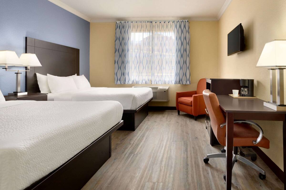 Ein Hotelzimmer mit zwei Betten, einem Schreibtisch, einem Stuhl, einem Fernseher und einem Fenster mit Vorhängen.
