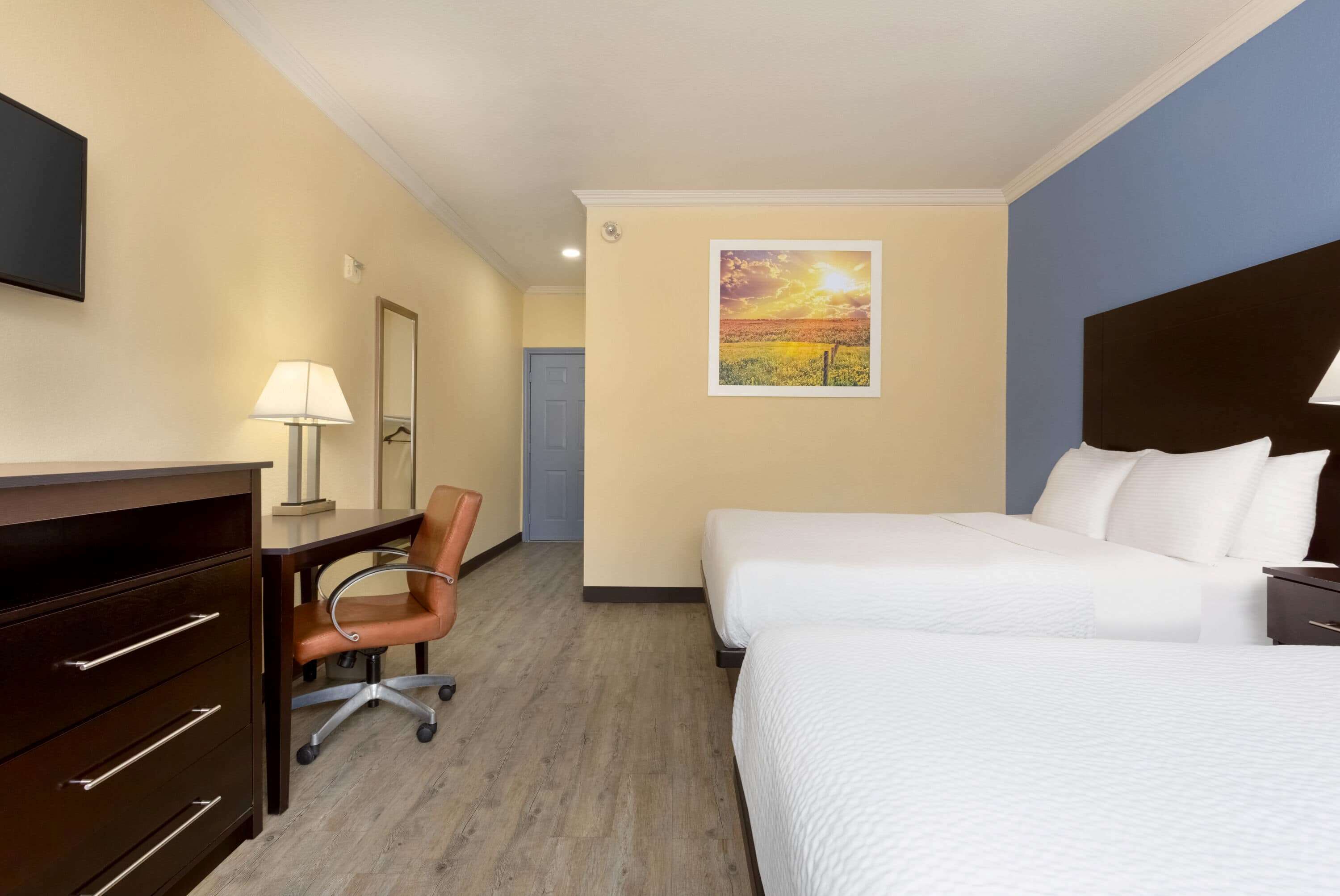 Une chambre d’hôtel avec deux lits, un bureau avec une chaise, une lampe et un tableau au mur.