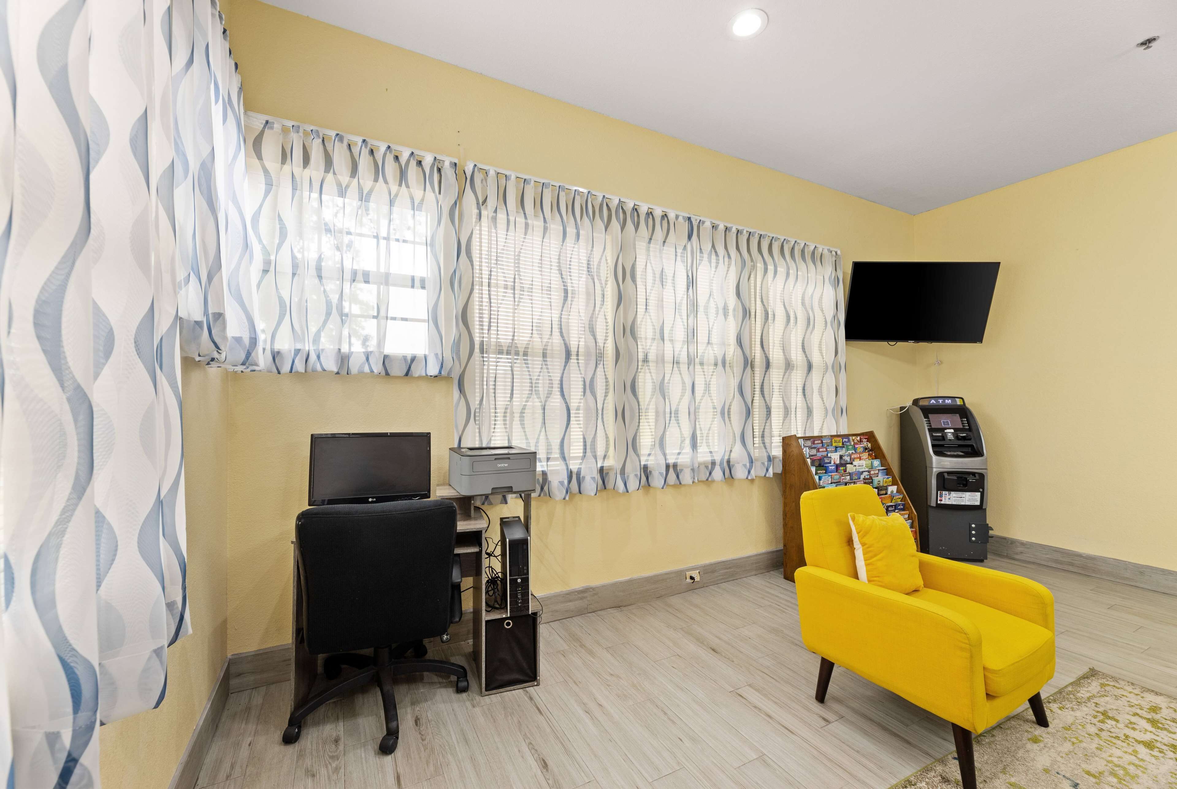 A room with a desk, a computer, a yellow armchair, a television, and an ATM.
