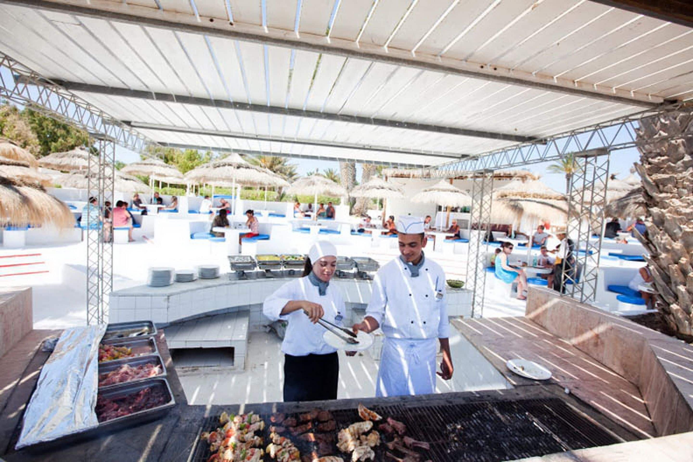 Un espace extérieur abrité, aménagé pour les repas, avec un barbecue, des sièges et des parasols.