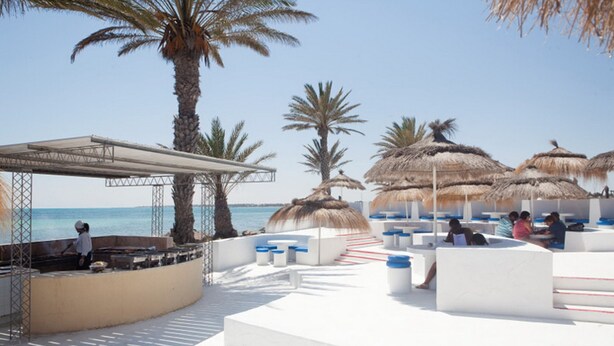 A beachside lounge with thatched umbrellas, palm trees, and a pool area. - El Mouradi Djerba Menzel (Aghir)