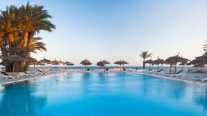 A swimming pool with lounge chairs and palm trees, overlooking the sea. - El Mouradi Djerba Menzel (Aghir)